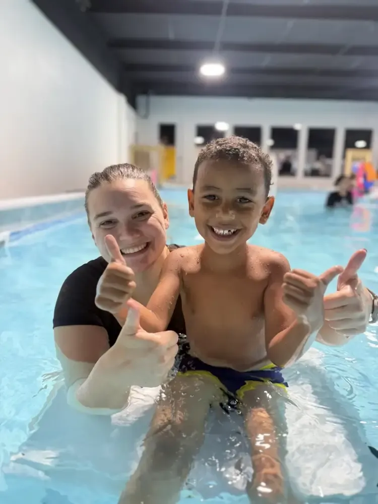 A Tiny Fins instructor and a school-aged boy giving a thumbs up in the pool