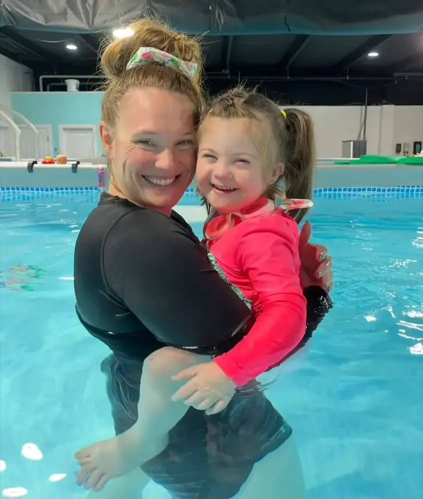 A Tiny Fins instructor holding a smiling toddler in the pool