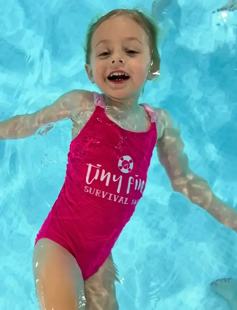 A young girl in a Tiny Fins swimsuit moving through the water