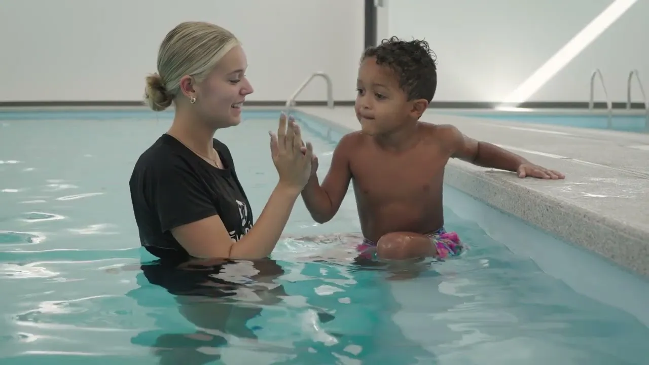 A Tiny Fins instructor high-fives a young boy sitting on the edge of the Springfield pool